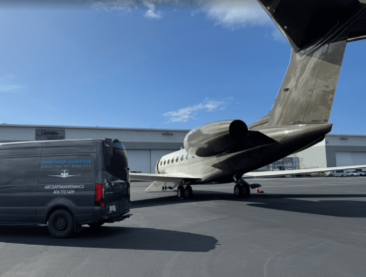 A private jet and a black van on an airport tarmac under a blue sky.