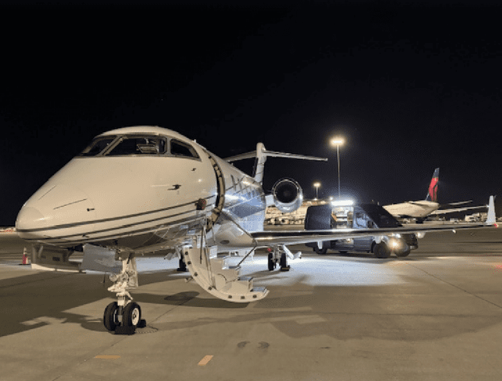 Private jets lined up on a dimly lit airport tarmac at night.